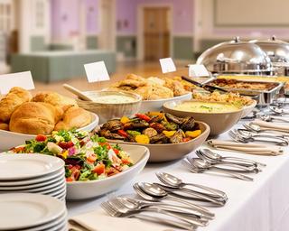 Large community hall buffet bundle with serving utensils and labelled dishes laid out for guests